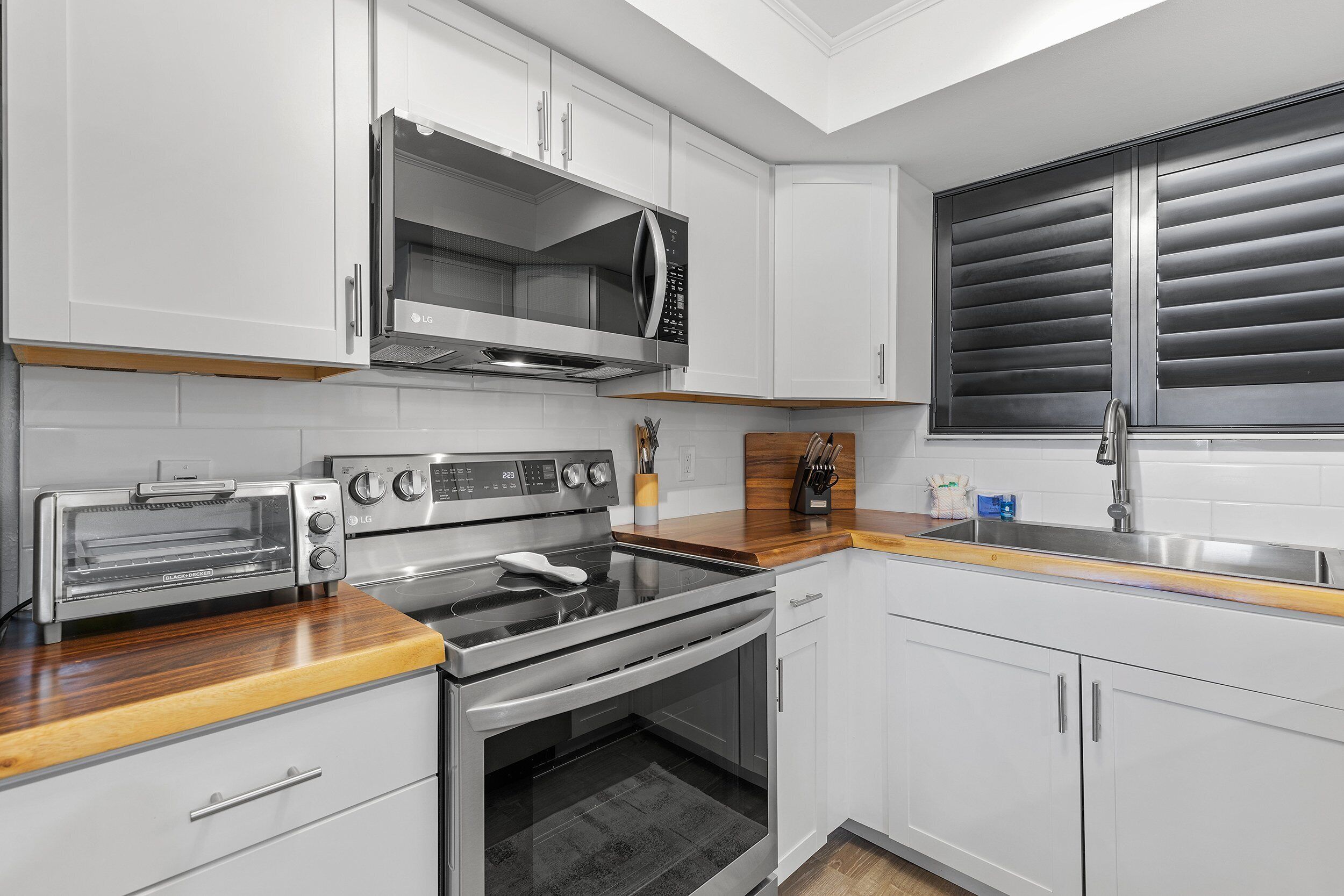 A modern kitchen with white cabinets, a stainless steel range, a built-in microwave, and a toaster oven.
