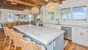 A modern kitchen with a large island, white cabinetry, and a view of the ocean. - Oceanfront Beach House, Elevator to First Floor, Ocean View Pool, Dog Friendly (Pawleys Island)