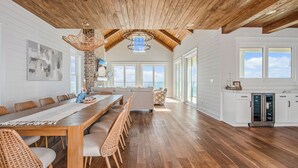 A spacious kitchen with a long wooden table and chairs, a brick wall, and large windows. - Oceanfront Beach House, Elevator to First Floor, Ocean View Pool, Dog Friendly (Pawleys Island)