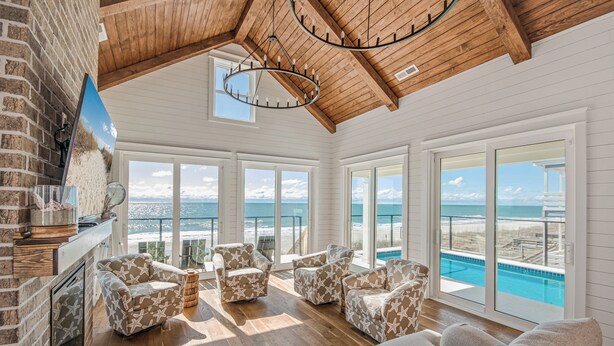 A spacious living room with a wooden ceiling, large windows, and a view of the ocean. - Oceanfront Beach House, Elevator to First Floor, Ocean View Pool, Dog Friendly (Pawleys Island)
