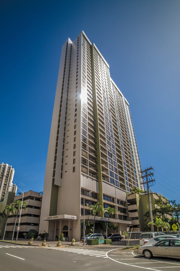A tall, modern building with multiple floors and a prominent entrance. - Waikiki Sunset Close to Beach with Parking (Honolulu)