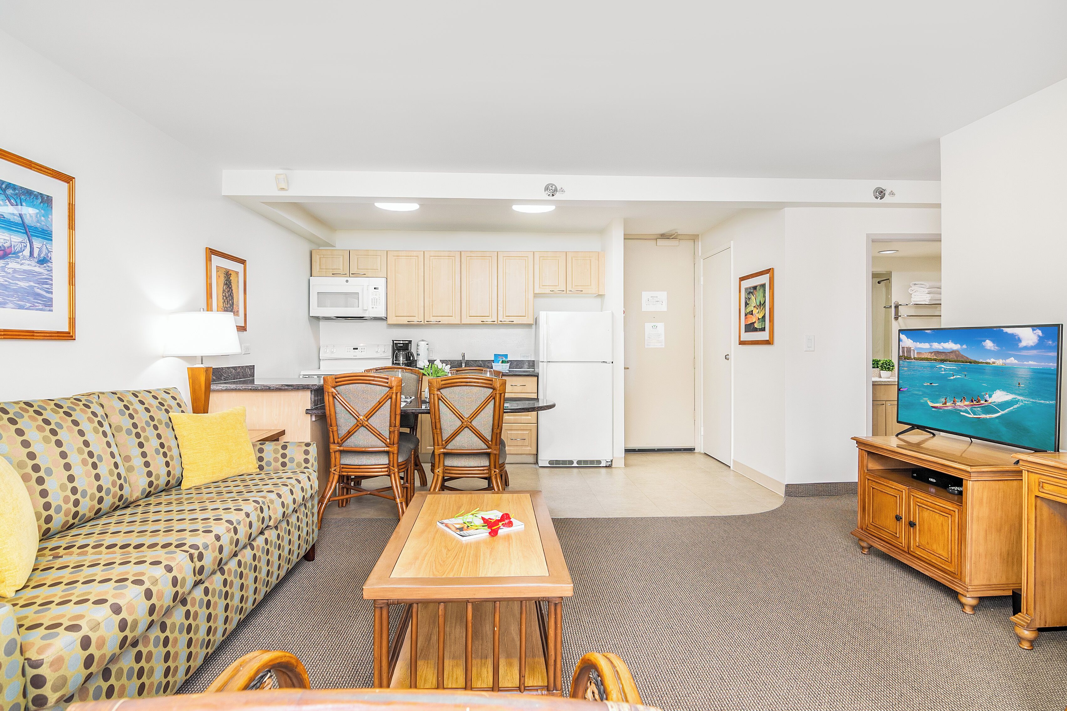 A living room with a sofa, dining table, chairs, a TV, and a kitchen area with cabinets and appliances.