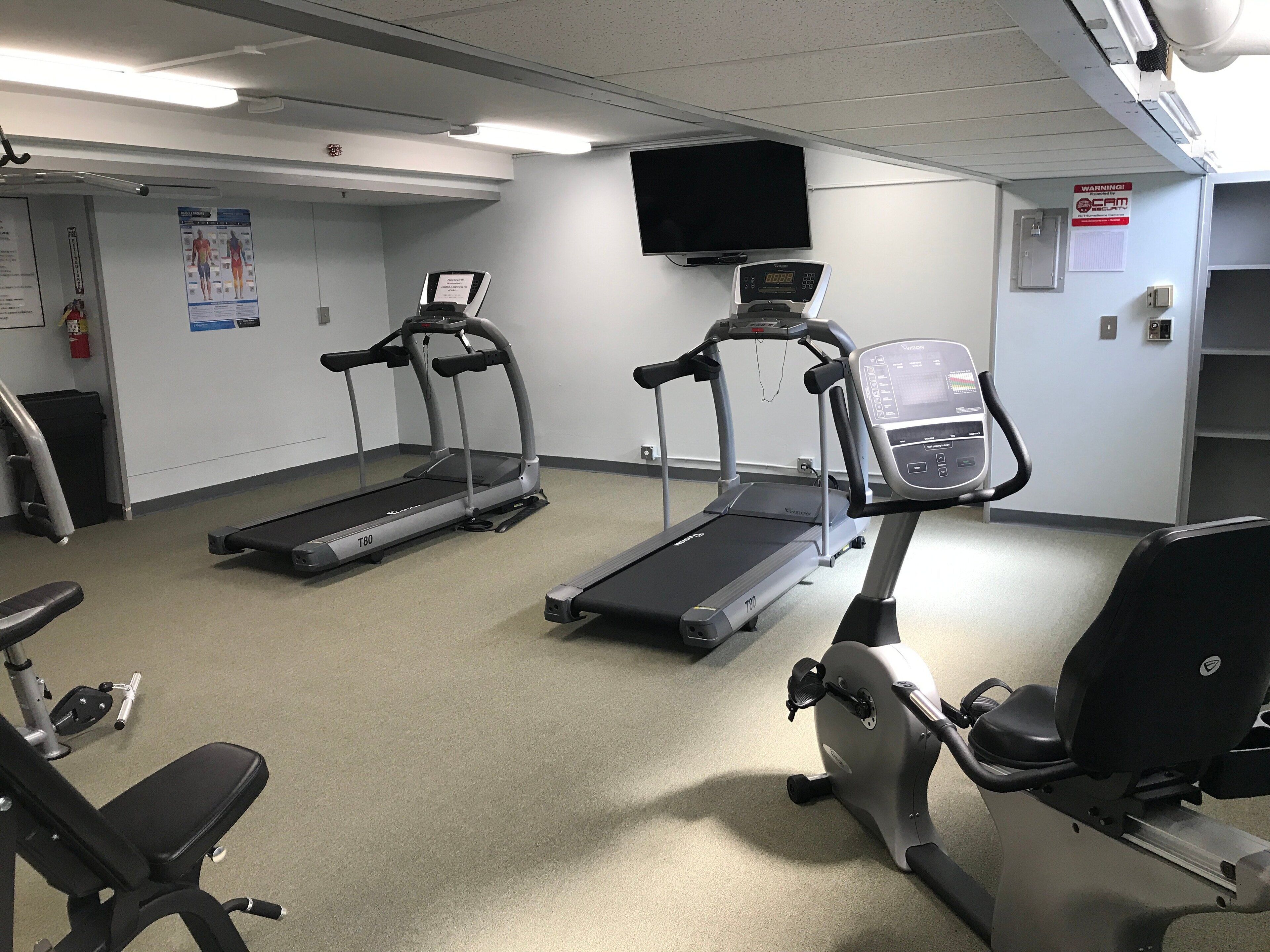 A fitness room with treadmills, a stationary bike, and a bench.