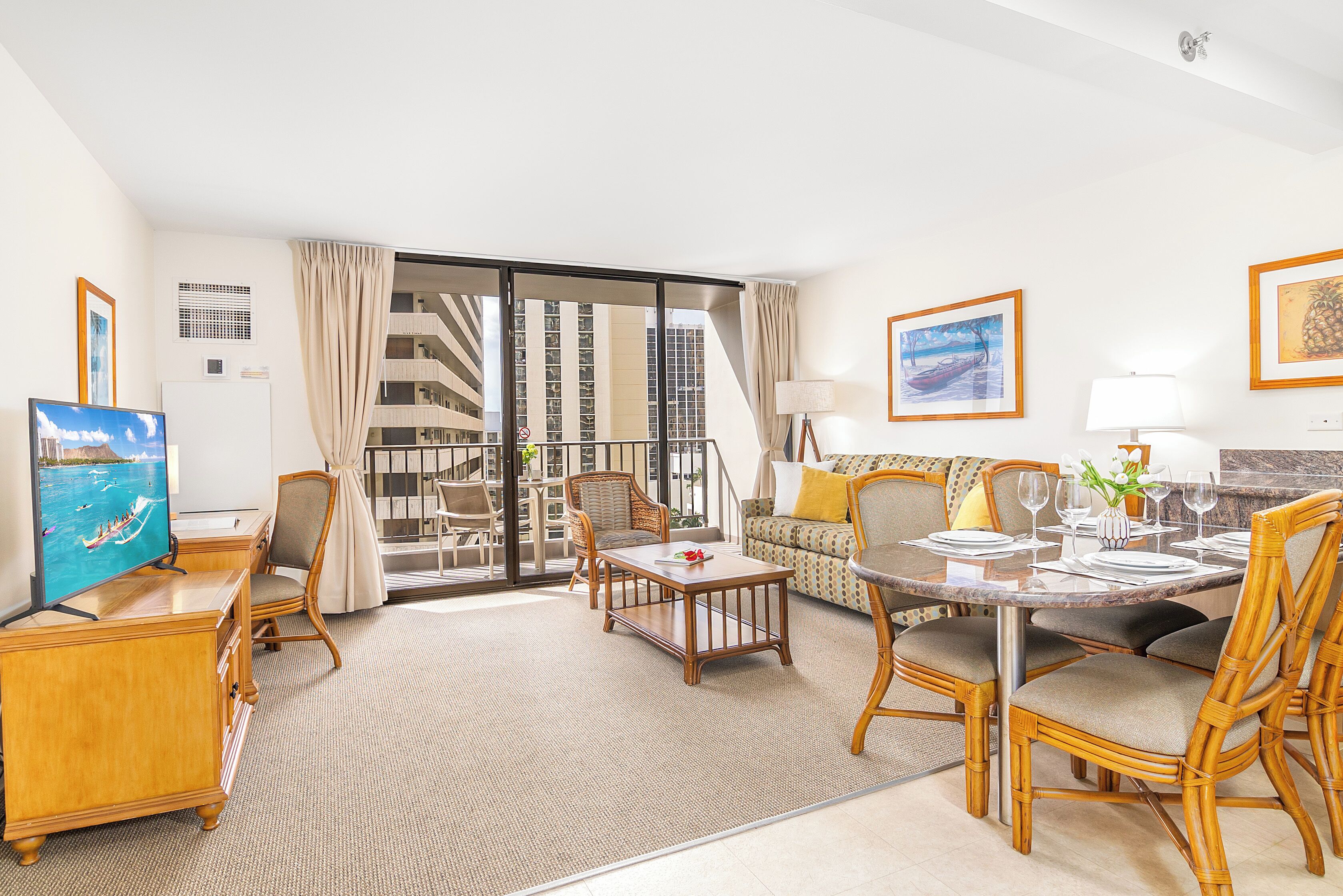 Quarto de hotel com área de jantar, televisão, sofá e varanda com vista para edifícios altos.