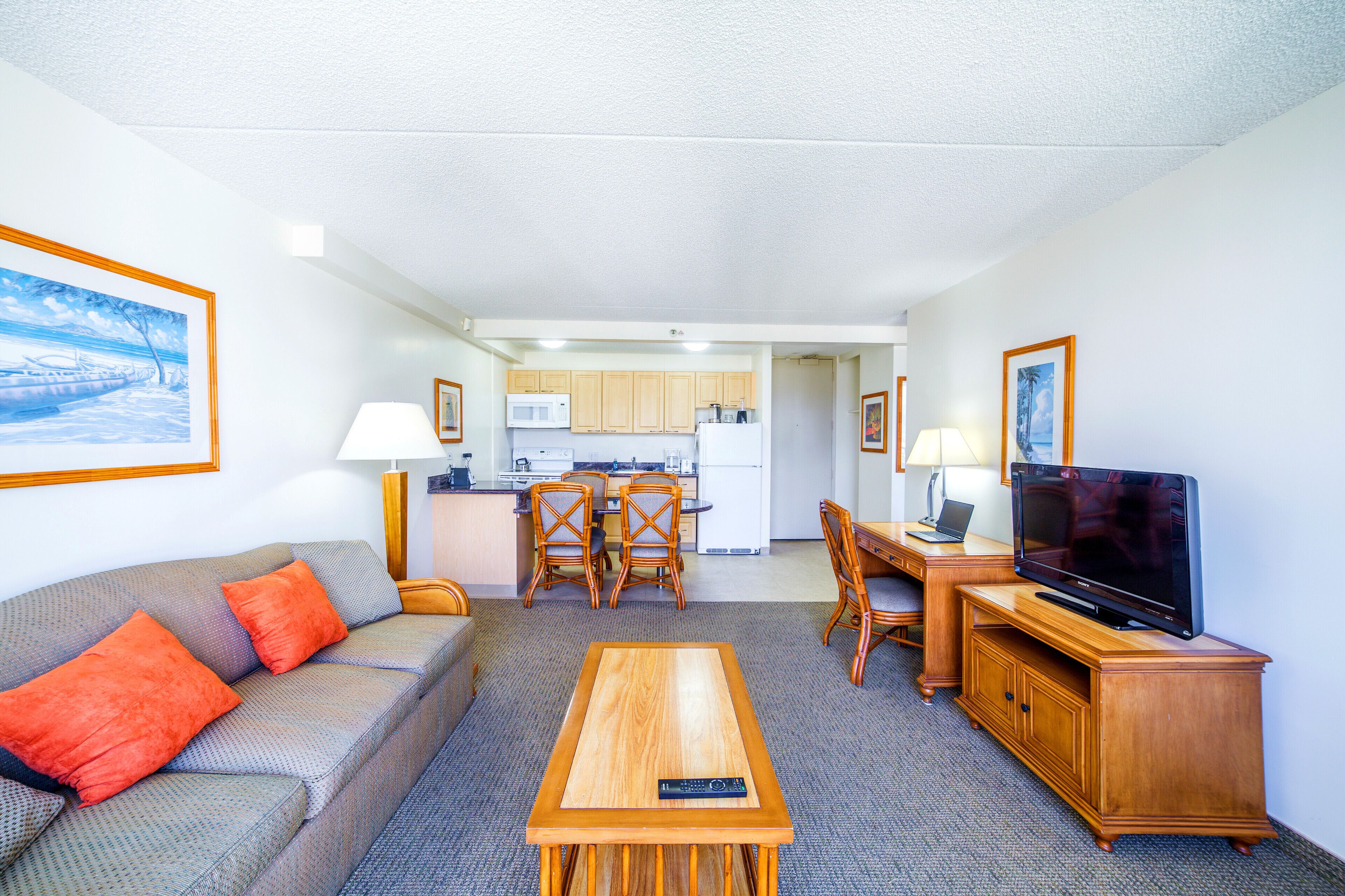 A compact living space with a sofa, a coffee table, a TV, a dining table, and a kitchen area.