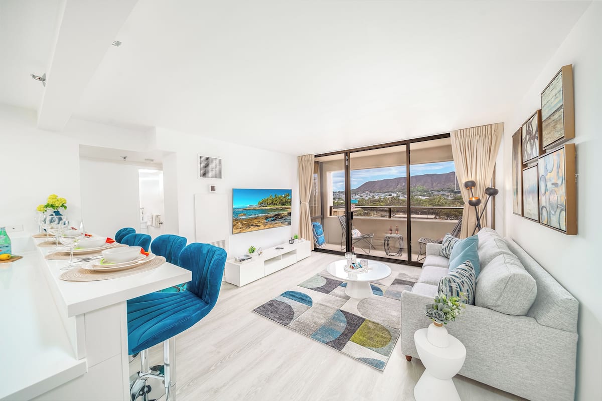 A modern living room with a dining area, large windows, and a view of a mountainous landscape.