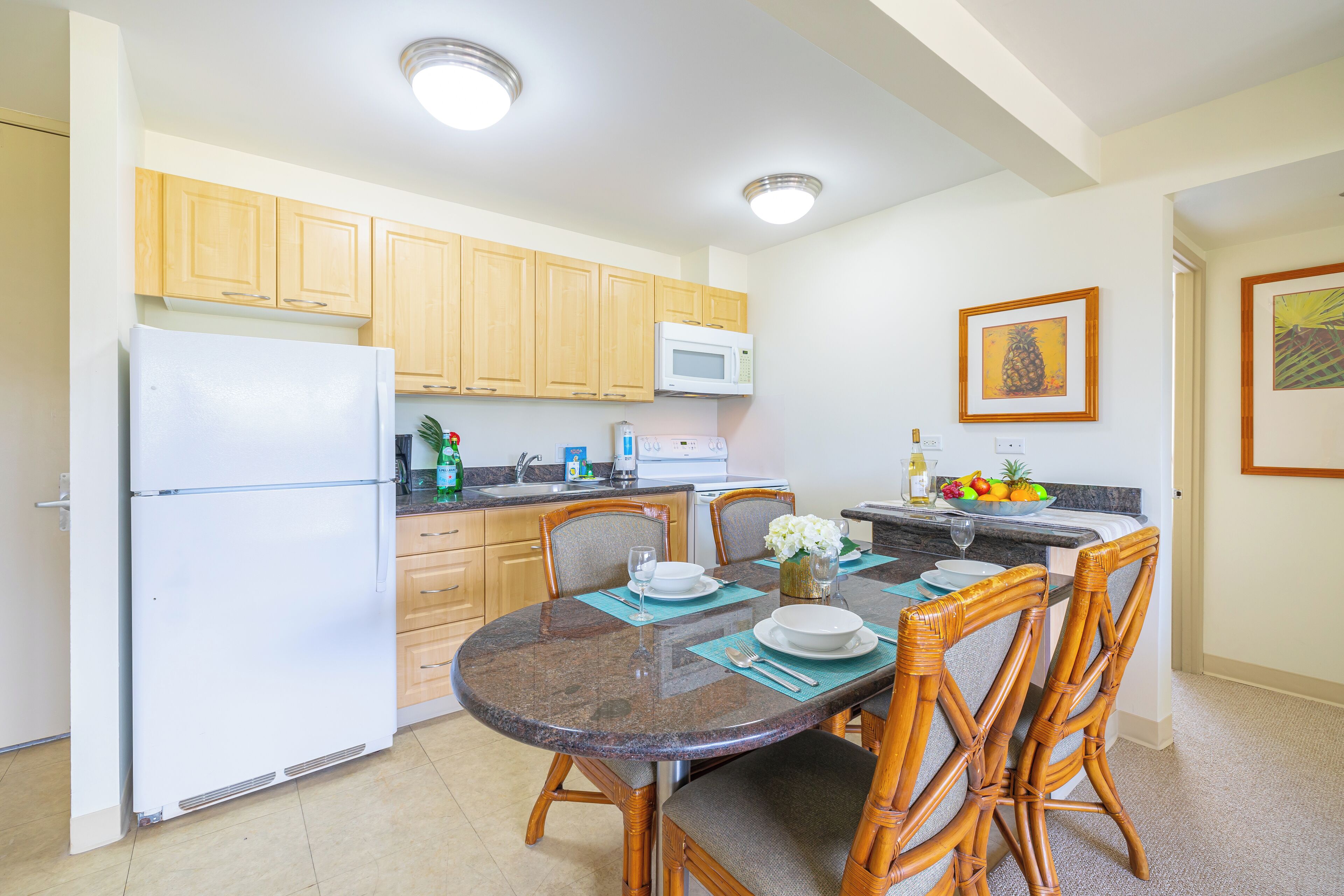 Una cocina compacta con armarios de madera, un refrigerador blanco, un microondas y una mesa de comedor con sillas.