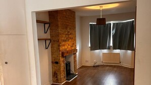 A spacious room with hardwood flooring, a brick fireplace, and a large window with curtains. - Chatham Retreat by the River (Chatham)
