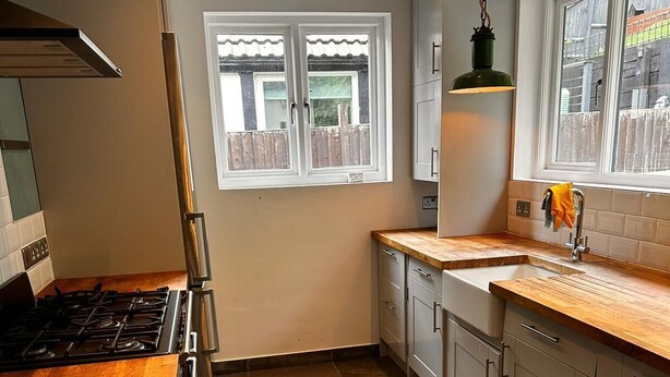 A kitchen with a wooden countertop, a gas stove, a window with a view of a fence, and a hanging light fixture. - Chatham Retreat by the River (Chatham)