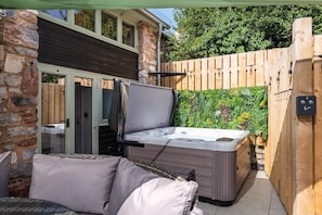 A hot tub in a backyard with a wooden fence and a stone wall.