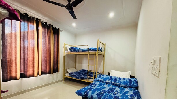 A room with bunk beds, a ceiling fan, and a window with curtains. - Prafull Hotel (Baijnath)