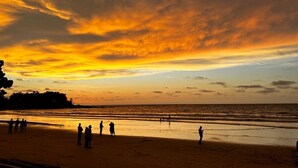 Escena de playa con gente y un atardecer.