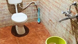 Un baño con inodoro, calentador de agua y un cubo verde.