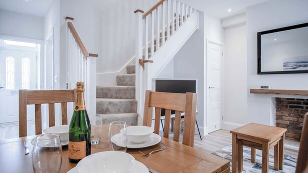 Un comedor con una mesa de madera preparada para cuatro personas, una botella de champán y una chimenea.