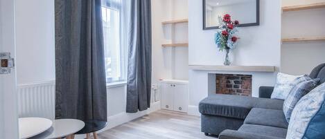 Ein modernes Wohnzimmer mit grauem Sofa, weißem Tisch und Kamin.