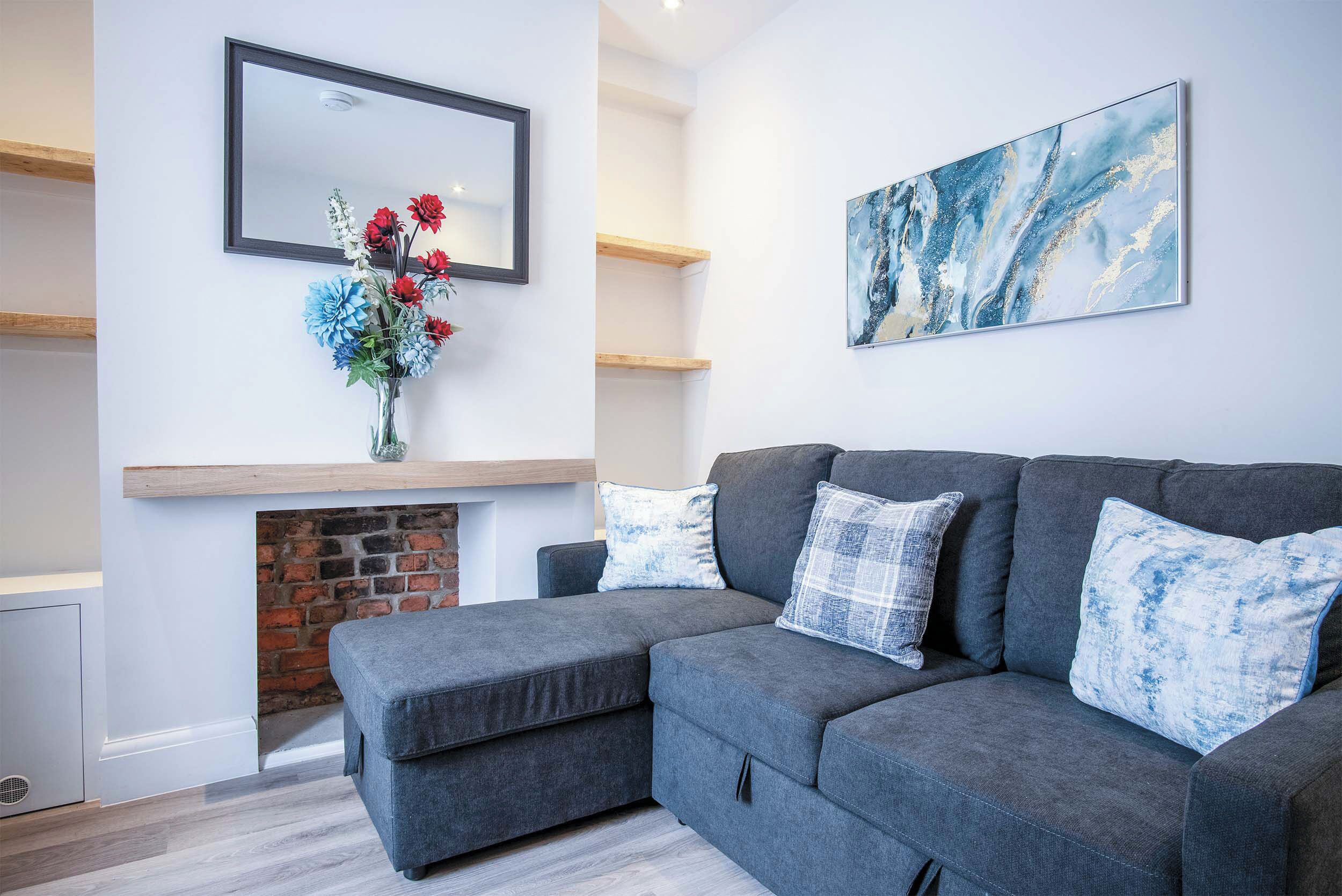 A modern living room with a grey sectional sofa, a fireplace, a mirror, and a large abstract painting.