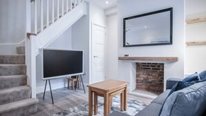 Una sala de estar moderna con una escalera, un televisor de pantalla plana, una chimenea y un sofá gris.