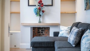 Una sala de estar moderna con un sofá gris, una chimenea y un jarrón con flores sobre la repisa.