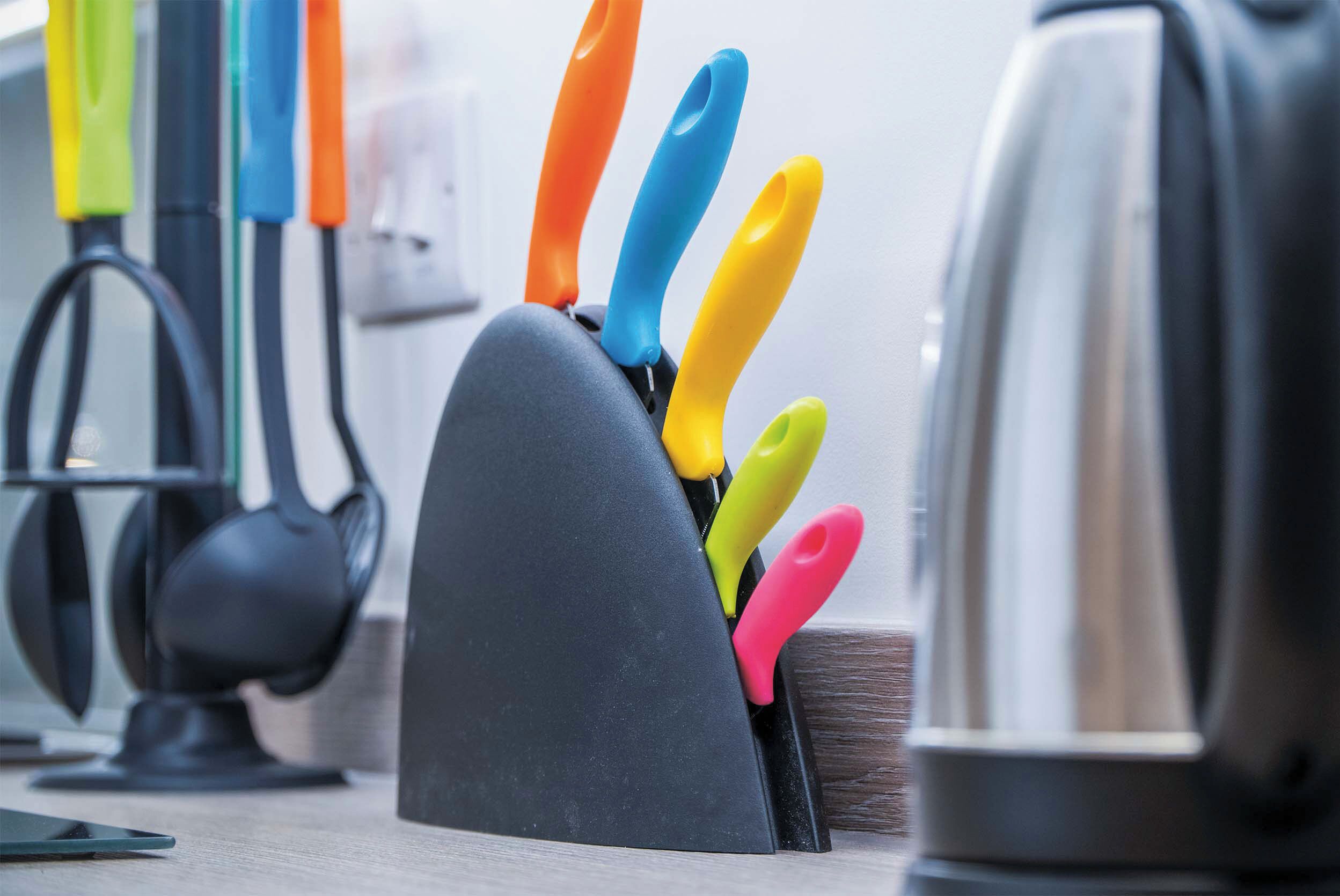 A kitchen counter with a knife holder containing various colored knives.