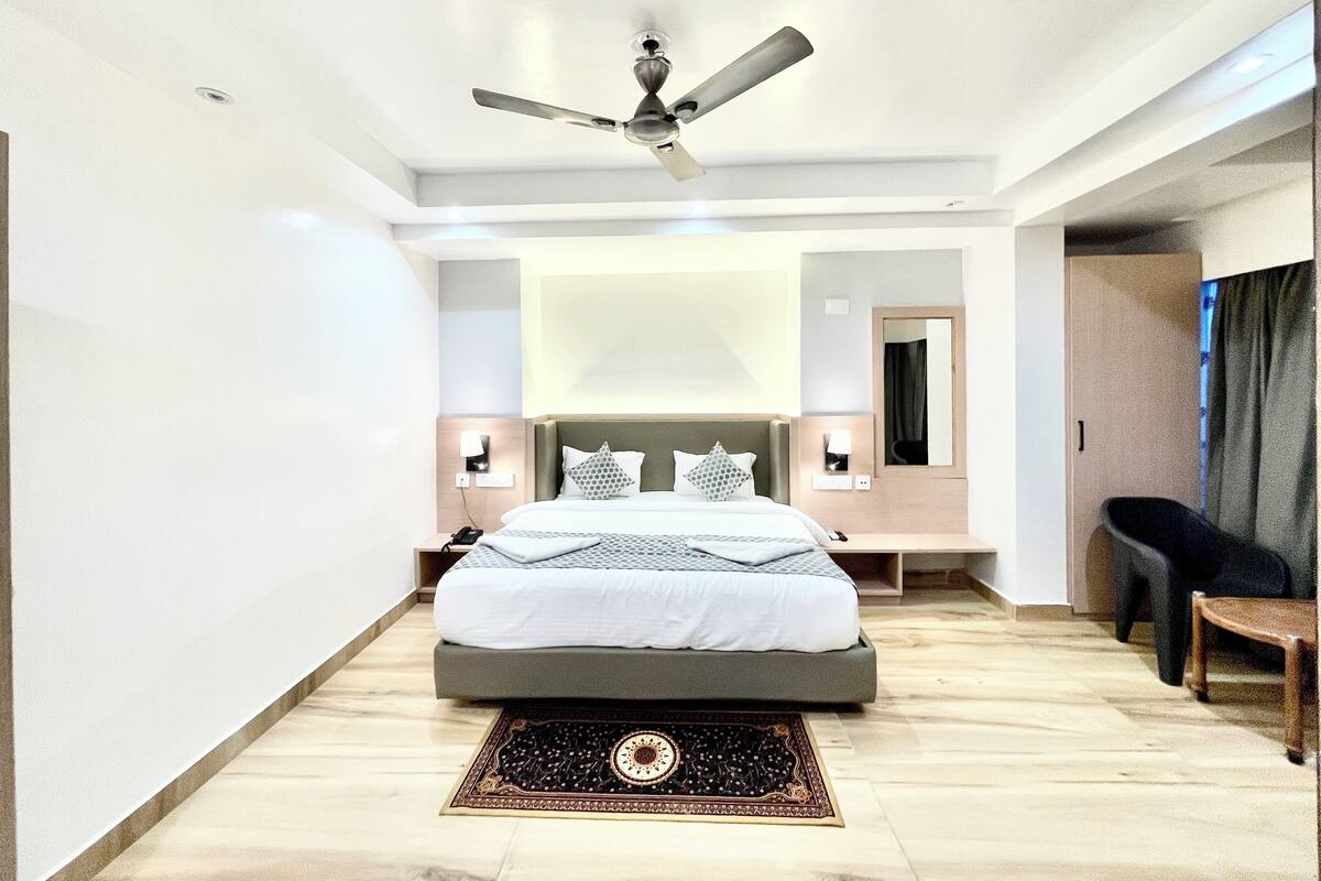 Une chambre d’hôtel moderne dotée d’un grand lit, d’un ventilateur de plafond, d’une table de chevet avec une lampe et d’un coin salon avec une chaise et une table.