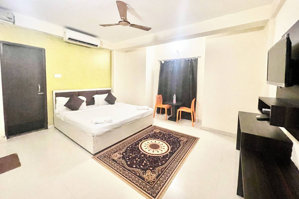 Une chambre d’hôtel équipée d’un lit, d’un ventilateur de plafond, d’un climatiseur, d’une télévision, d’un bureau et d’une chaise.