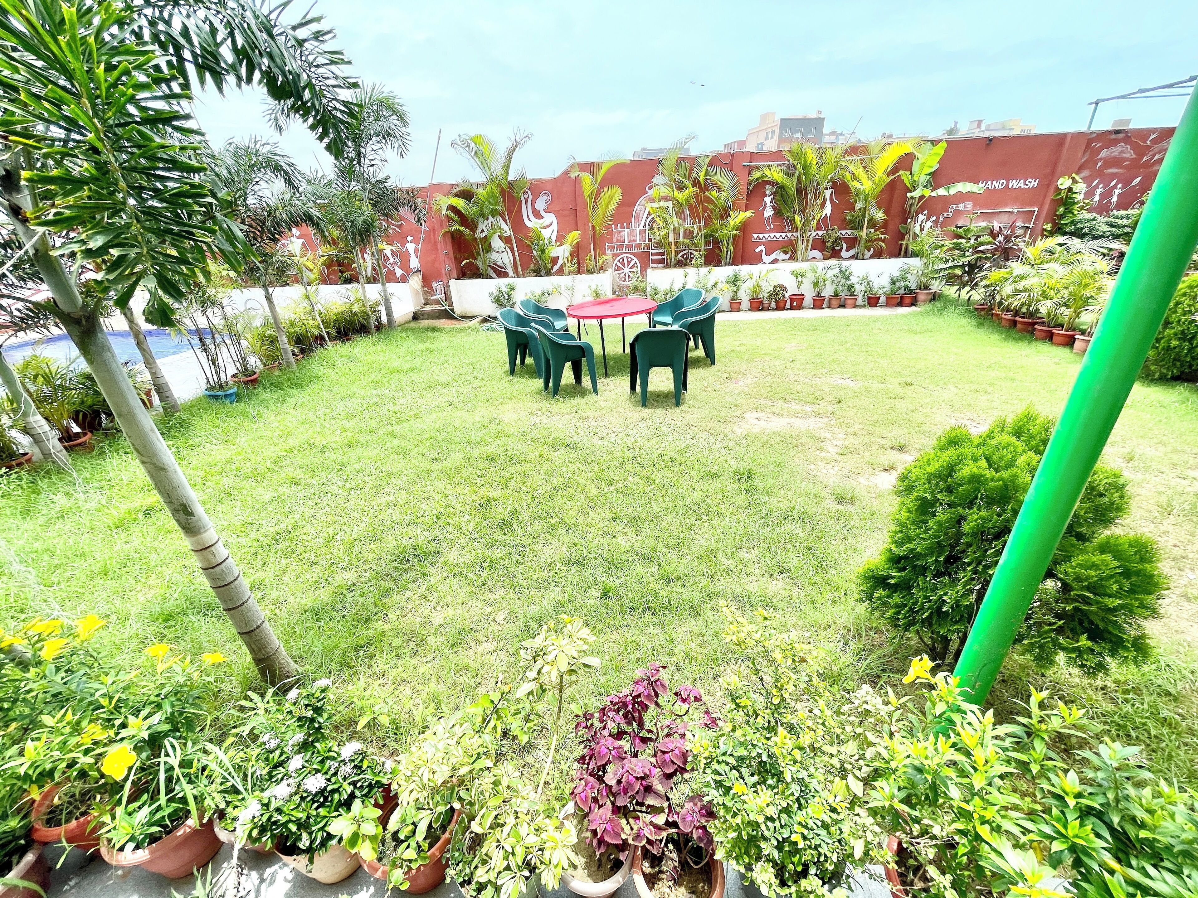 A grassy outdoor area with a table and chairs, surrounded by potted plants and trees.