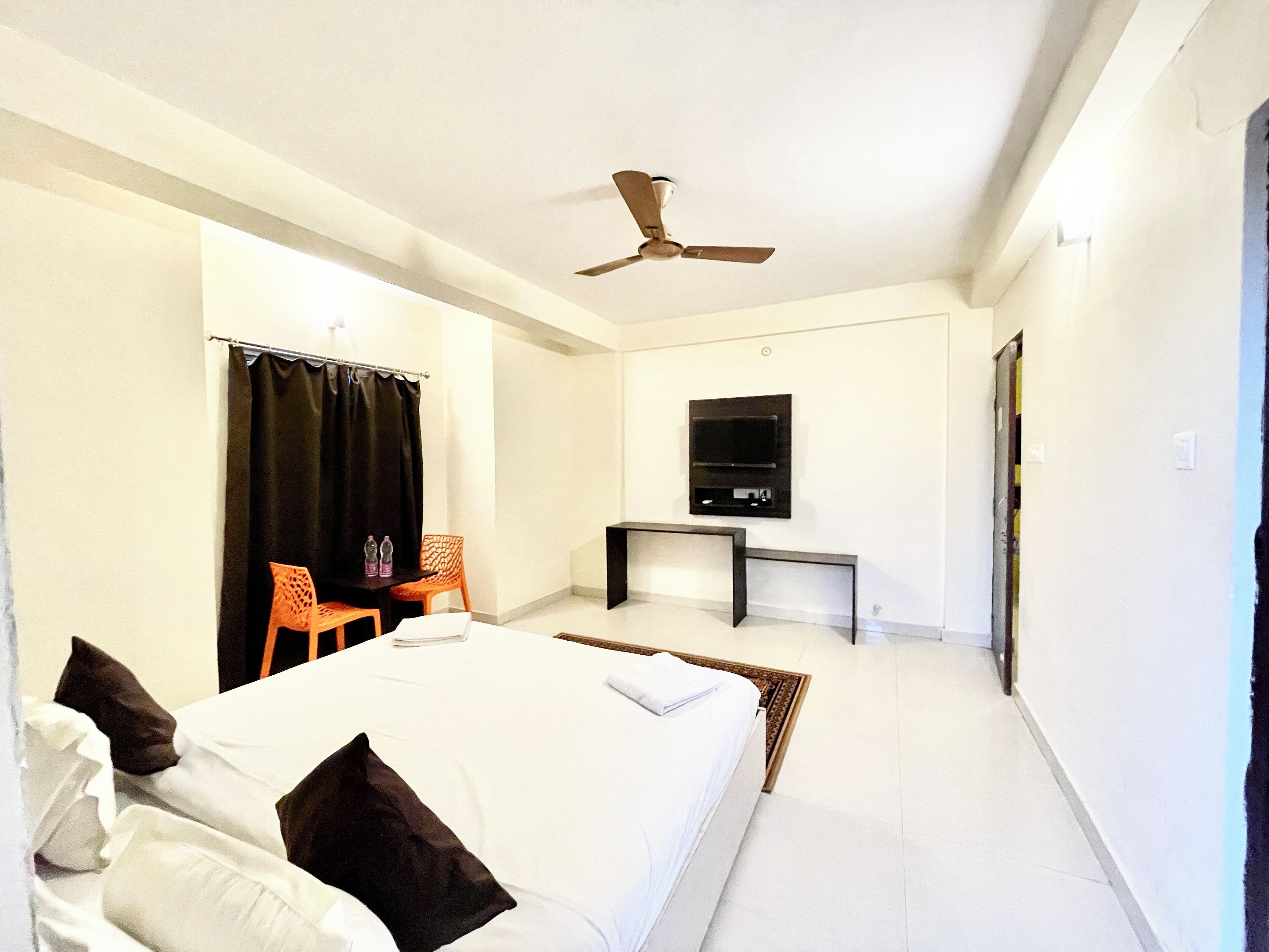 Ein Hotelzimmer mit Bett, Schreibtisch, Sessel, Fernseher und Deckenventilator.