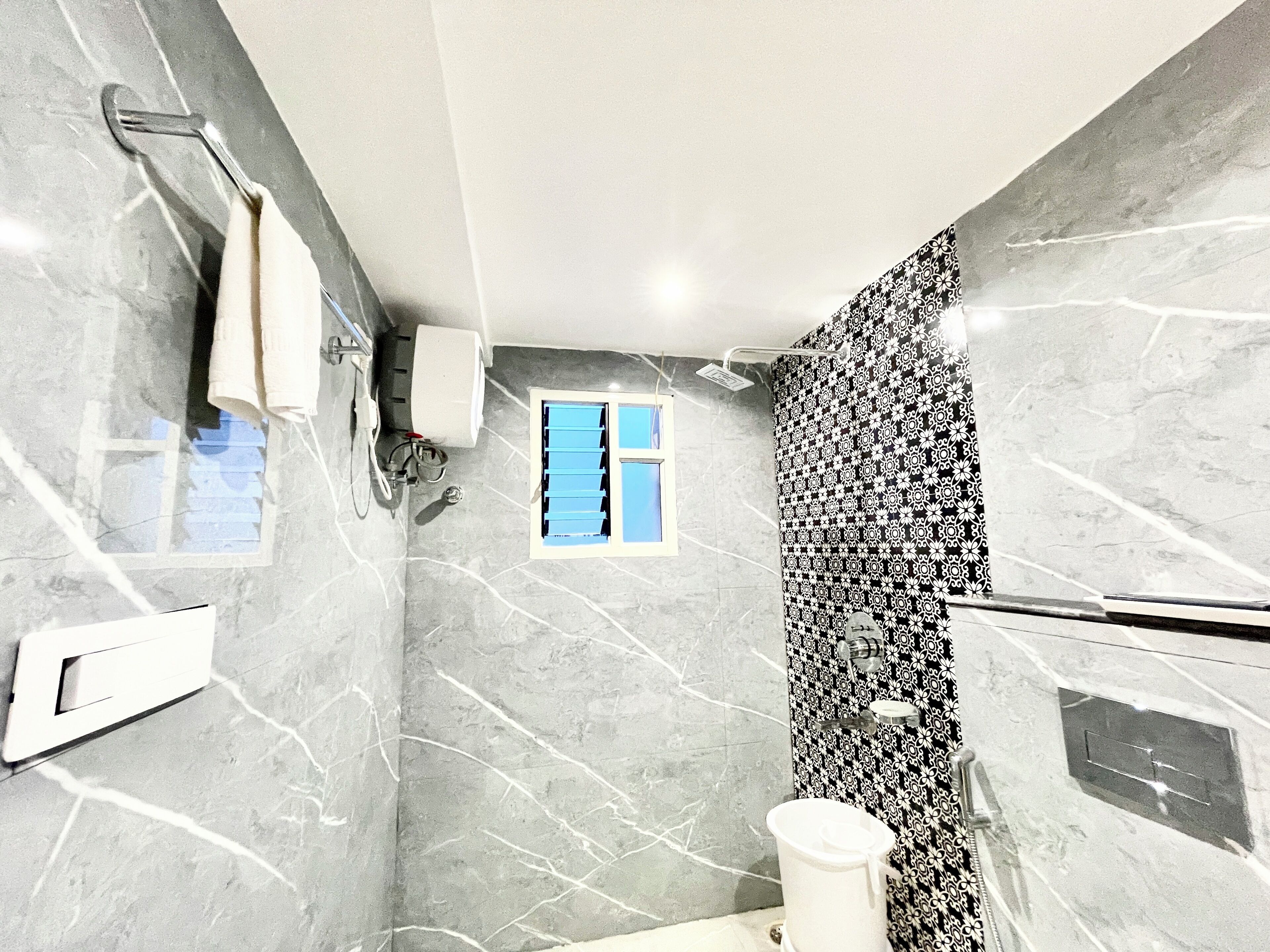 Un bagno con doccia, un water, un porta asciugamani e una finestra.