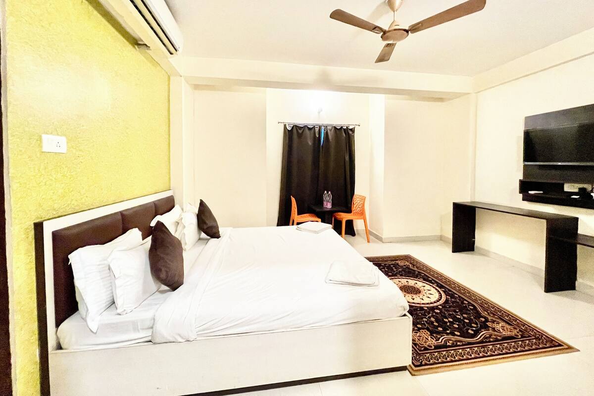 Une chambre à coucher avec un lit, un ventilateur de plafond, une télévision, un bureau et une chaise.
