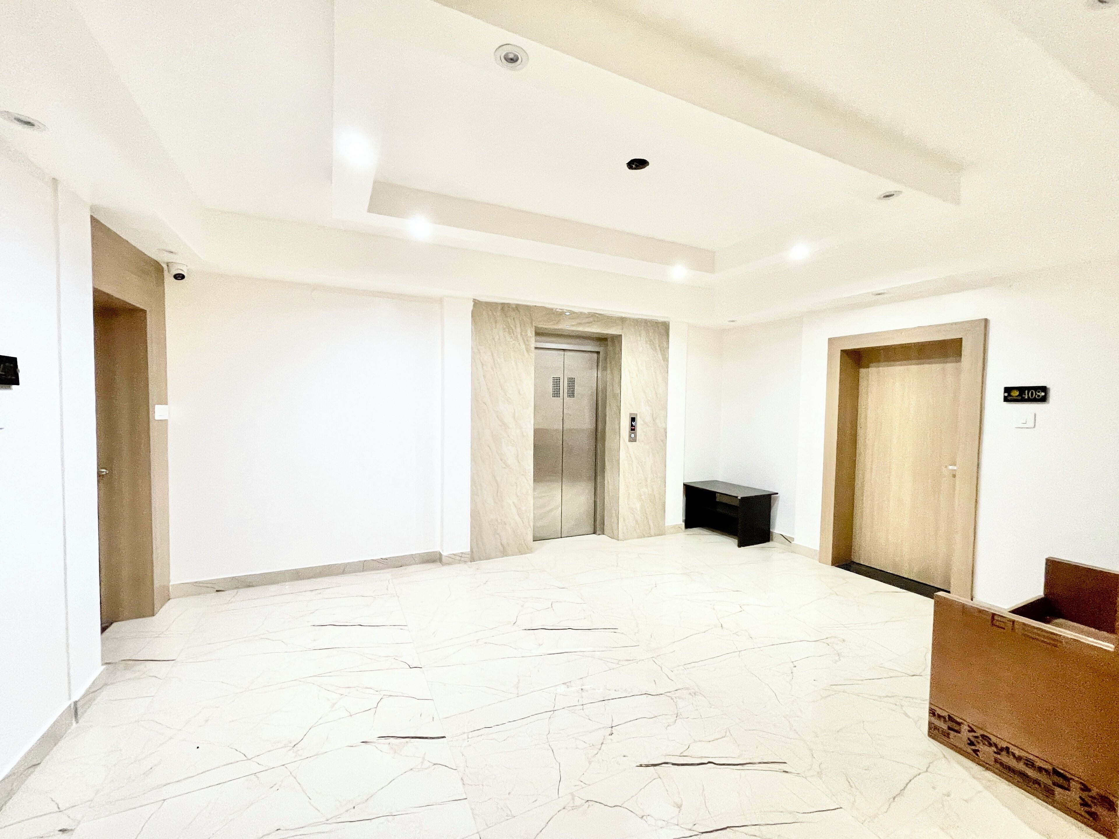 A spacious hallway with a marble floor, an elevator, and a reception desk.