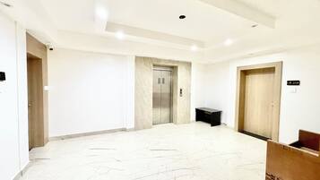A spacious hallway with a marble floor, an elevator, and a reception desk.