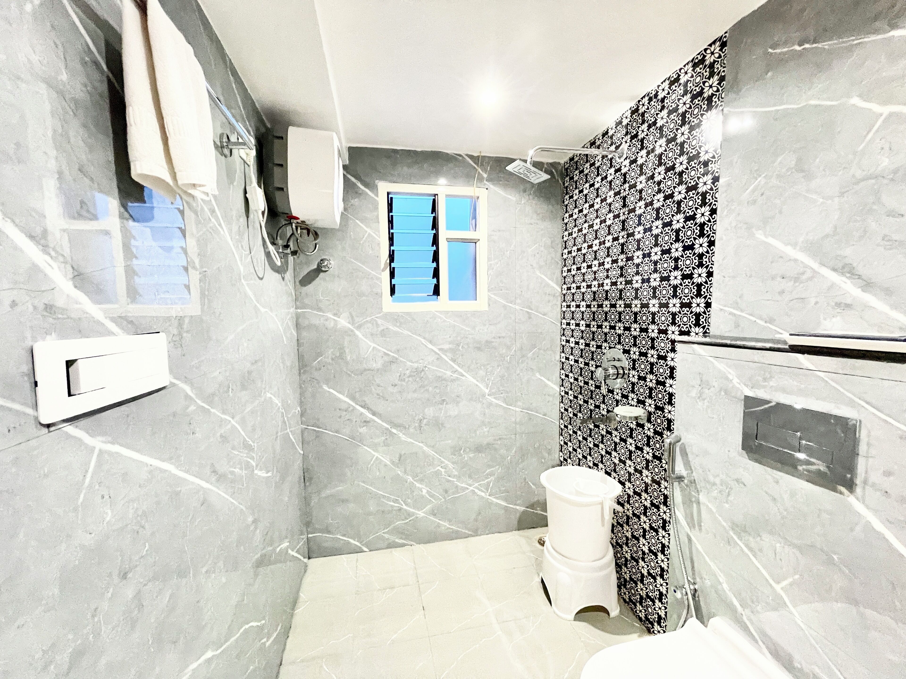 A bathroom with marble walls, a toilet, a shower, and a window with blue shutters.