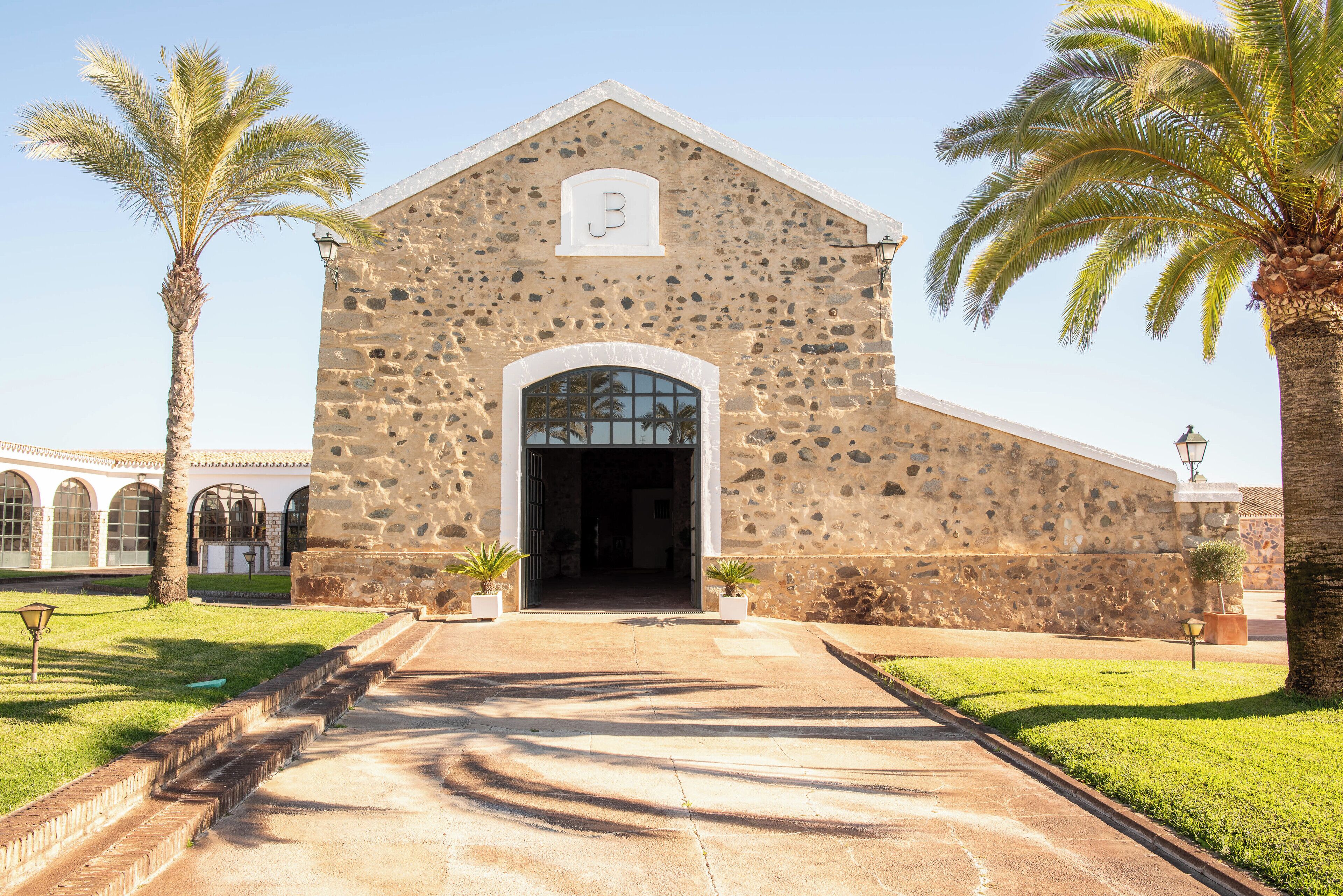 A stone building with a large arched entrance, palm trees, and a clear sky.