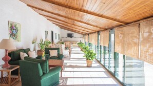 A sunlit indoor space with a wooden ceiling, green sofas, a TV, and potted plants. - HOTEL RURAL FINCA BARRAL (Guillena)