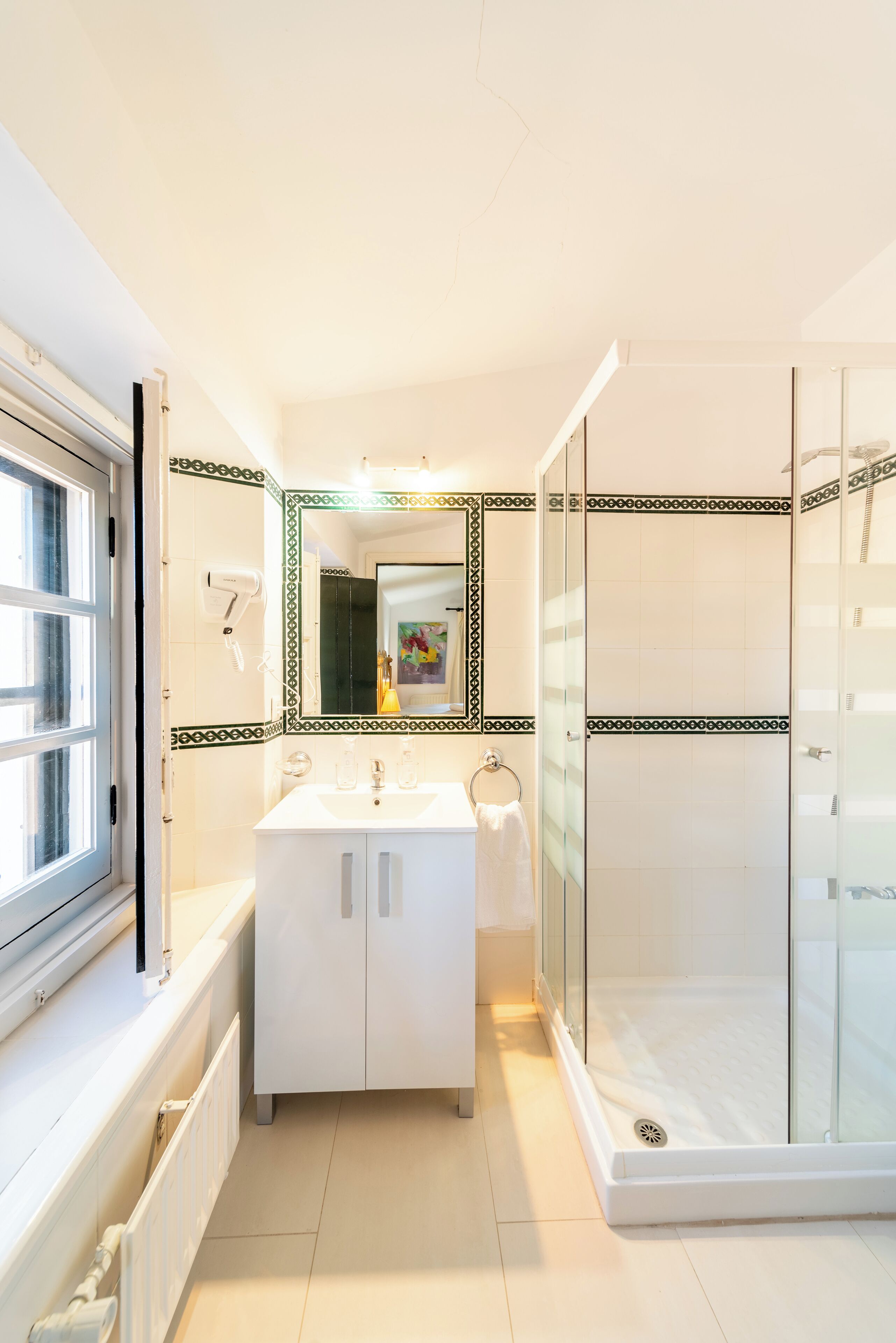 Un baño con tocador blanco, cabina de ducha con mampara de vidrio y un espejo grande con marco decorativo.