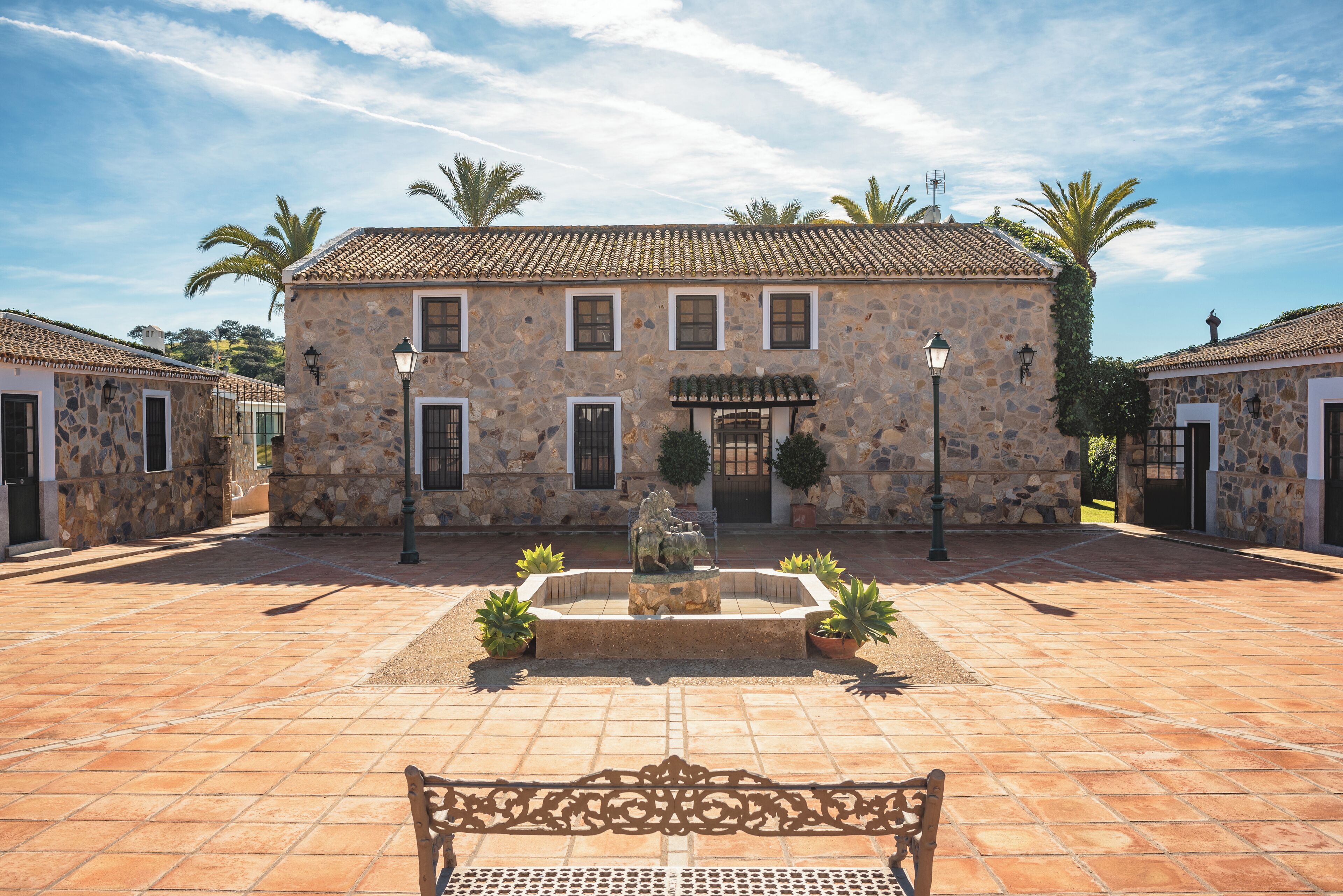 Un patio con un edificio de piedra, una fuente y plantas en macetas.