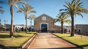 A building with a stone facade, a central entrance, and palm trees in the foreground. - HOTEL RURAL FINCA BARRAL (Guillena)