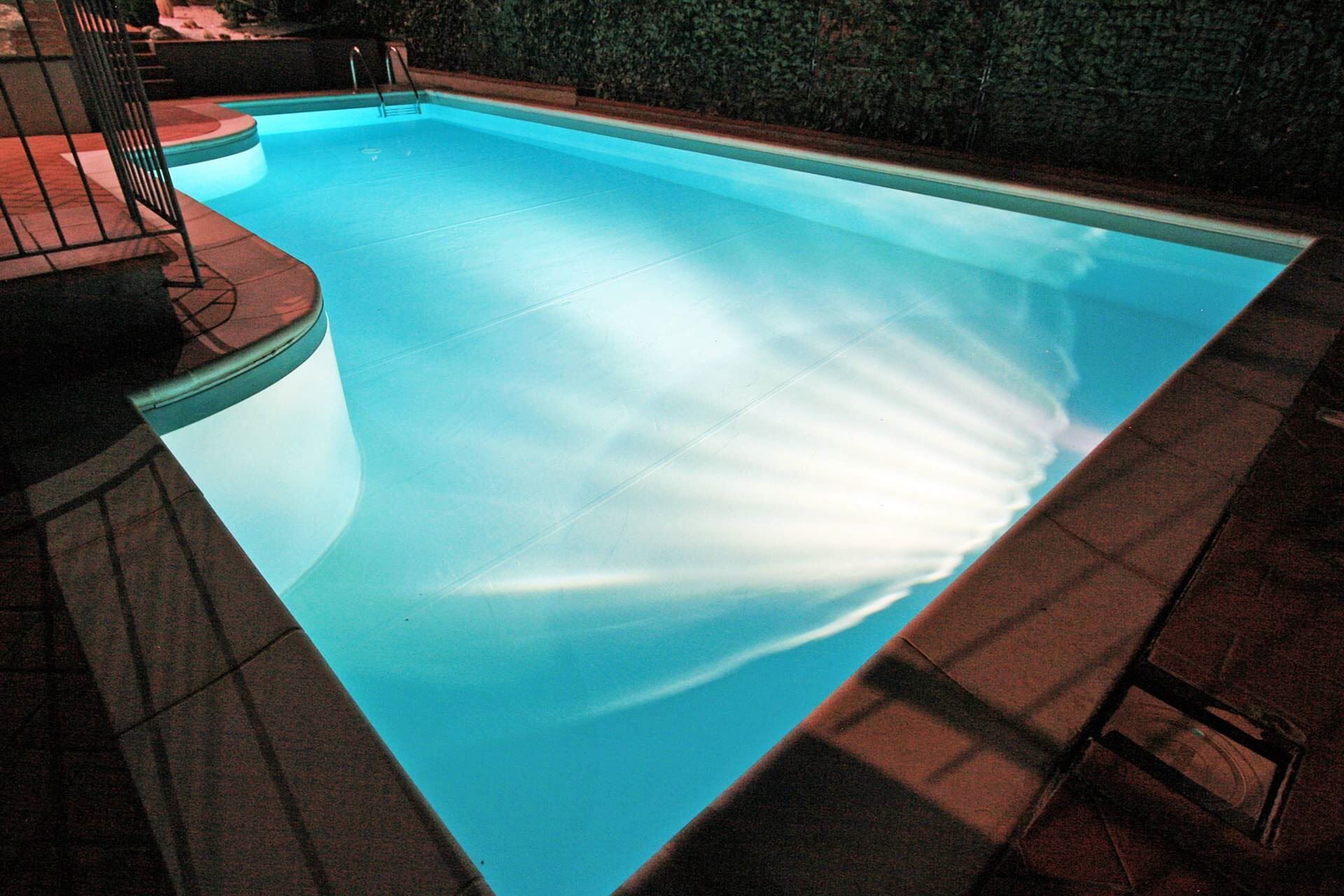 Una piscina amb una superfície d'aigua blava cristal·lina, envoltada per una paret de pedra i una tanca metàl·lica.