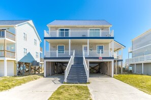 A multi-story beachfront building with a central staircase, balconies, and a garage entrance.
