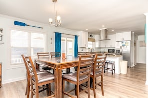 A modern kitchen with white cabinets, a stainless steel refrigerator, and a dining area with wooden chairs and a table.