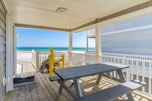 A covered deck with a table and chairs, overlooking a beach.