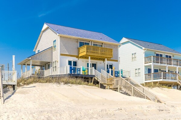 A beachfront house with a balcony, a covered porch, and a staircase leading to the entrance.
