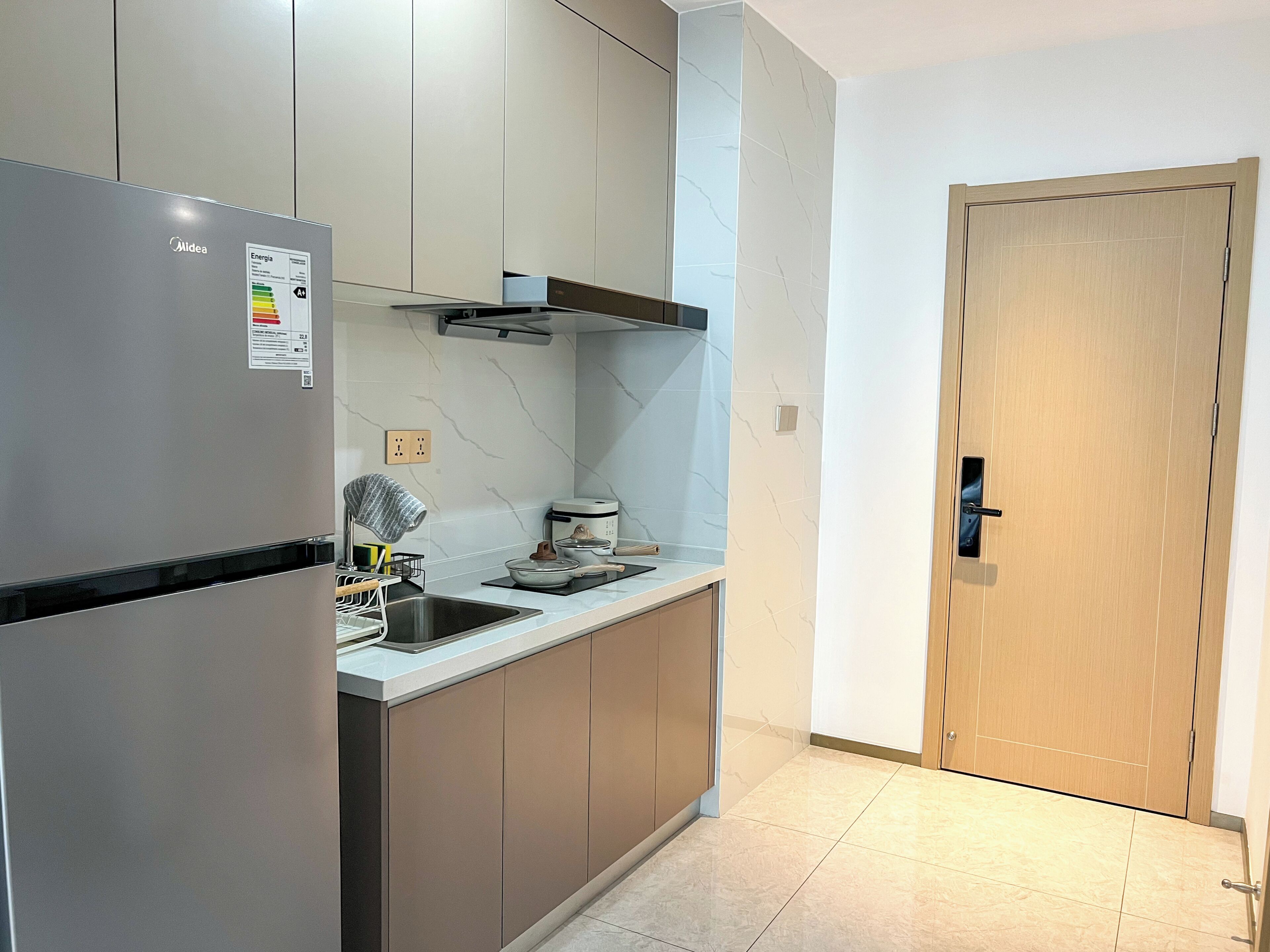 A modern kitchen with a built-in refrigerator, a stove, and a microwave. There is a wooden door to the right and a tiled floor.