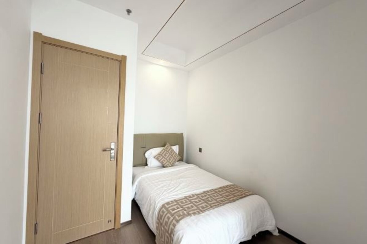 A single bed with a headboard, a wooden door, and a plain wall.