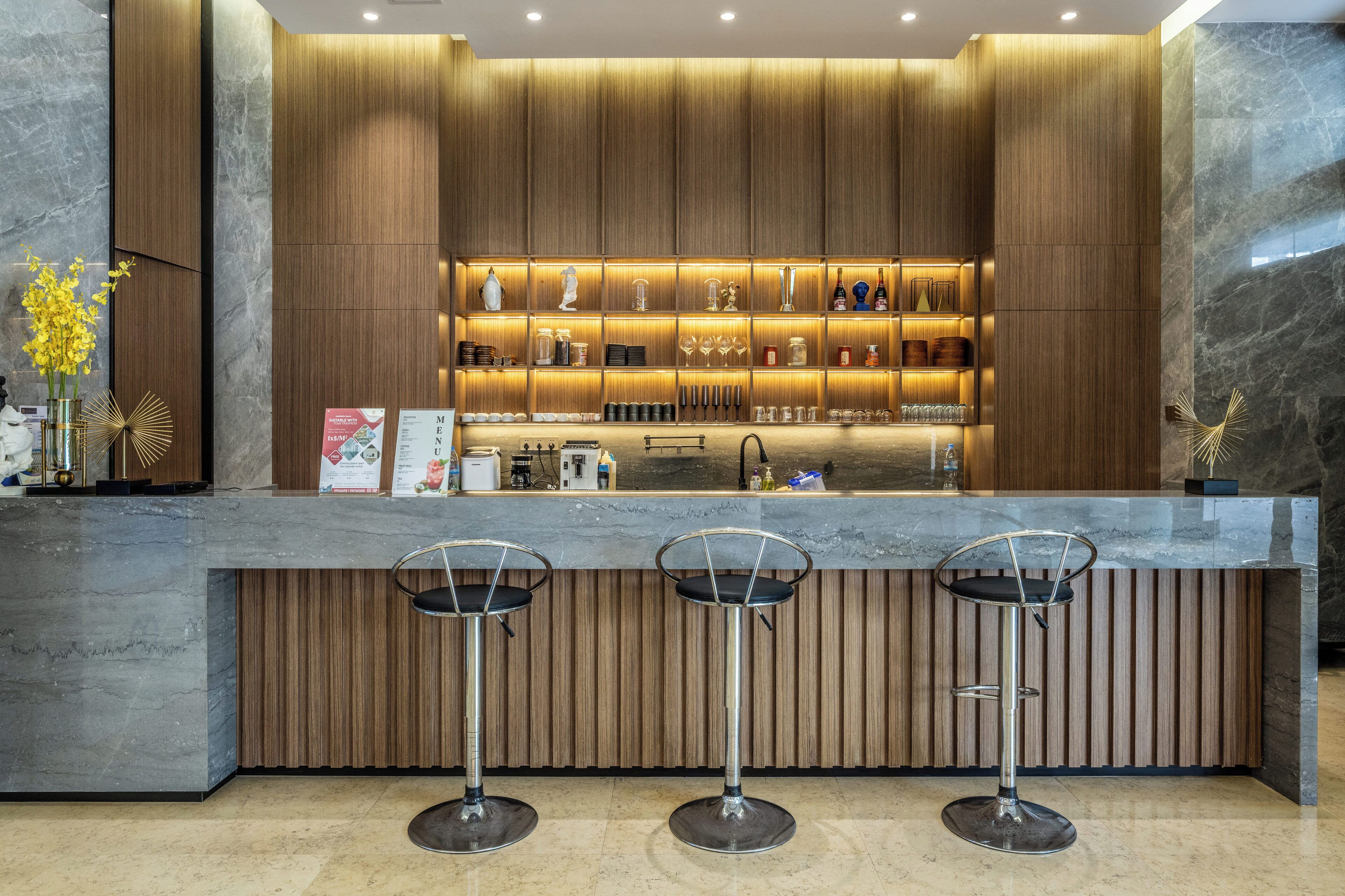 A modern bar area with a marble countertop, three bar stools, and a wooden panel backdrop.