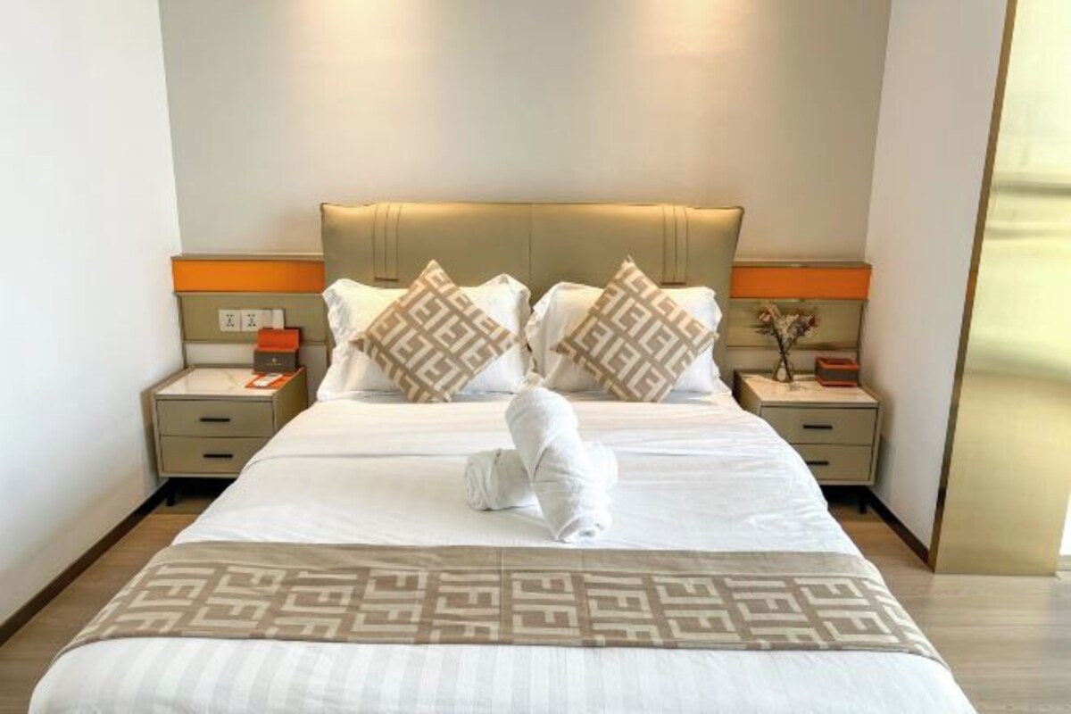 A neatly made bed with a patterned bedspread, two bedside tables with lamps, and a wall-mounted light fixture.