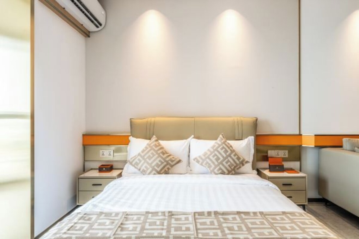 A hotel room with a bed, bedside tables, and a wall-mounted air conditioner.
