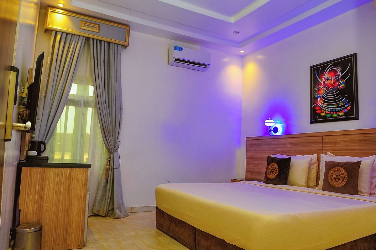 Habitación de hotel con cama, escritorio, basurero, aire acondicionado y un cuadro en la pared.