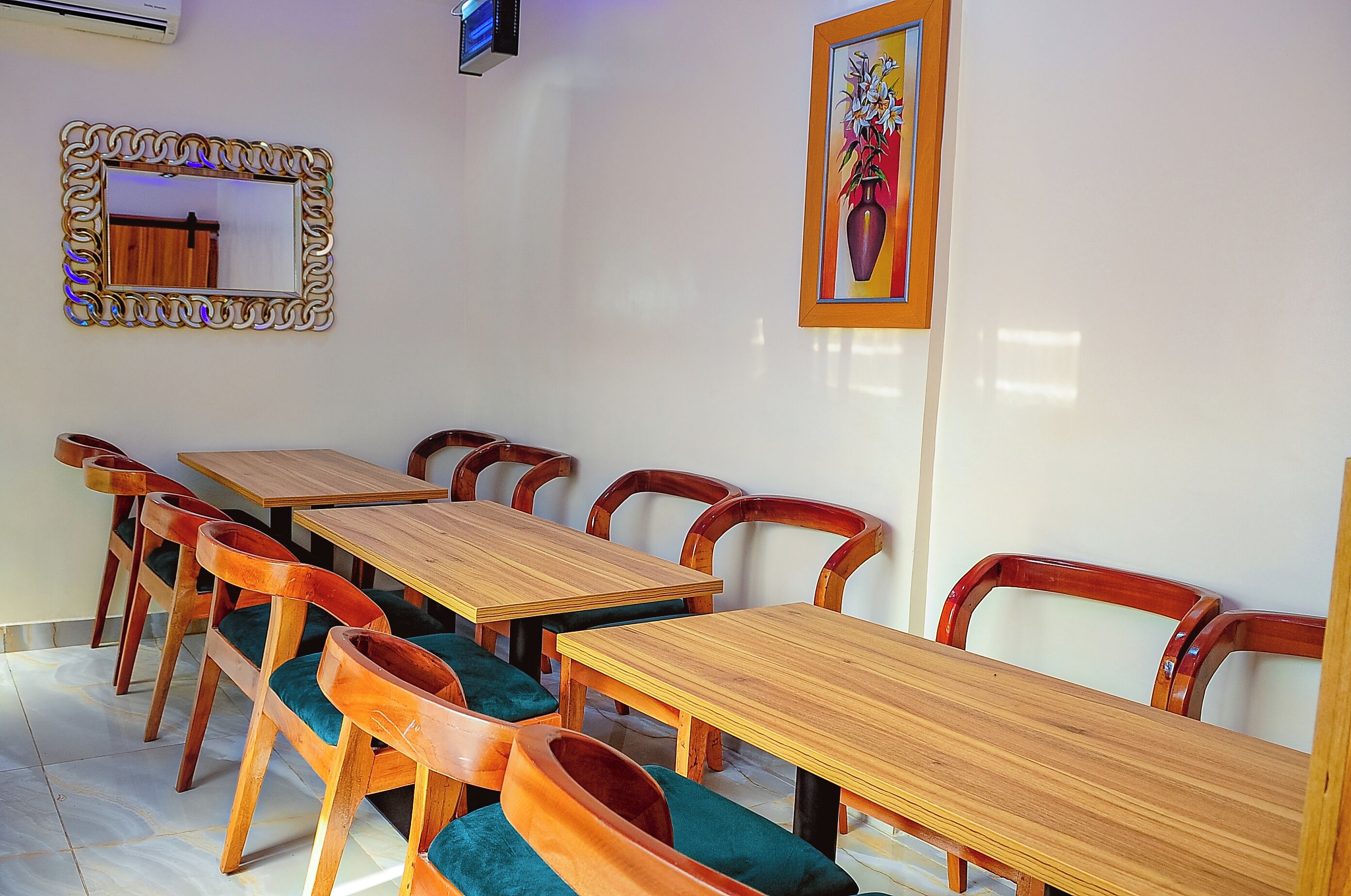 A dining area with wooden tables and chairs, a mirror, and a framed painting on the wall.