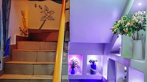 A staircase with a handrail, a wall with a leaf pattern, and shelves with vases and flowers. - Kashvalley Hotel and Suites (Lagos)